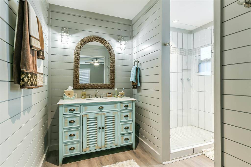 An ensuite featuring a designer vanity, complemented by wood-paneled walls and a ceramic-tiled enclosed shower.