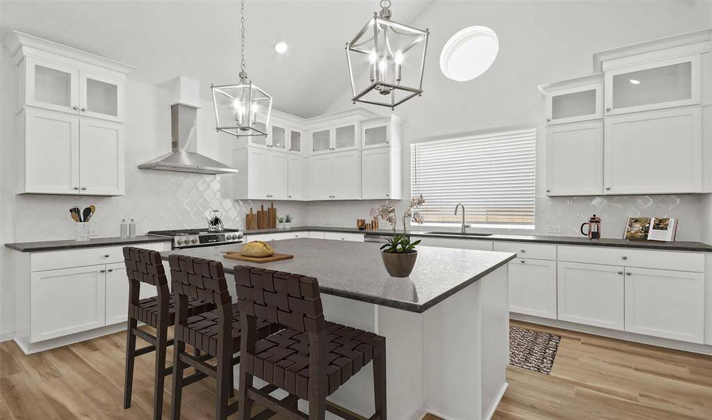 Steel Grey Brushed Granite countertops, Montana White cabinets with glass front tops, designed tile backsplash, and pendant lighting.