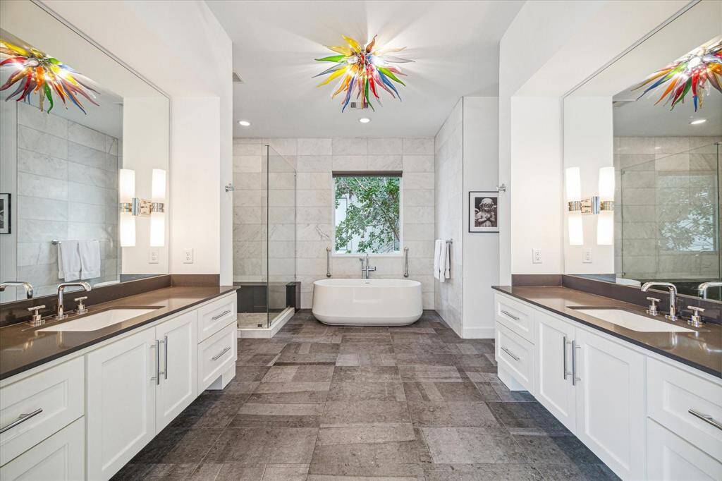 Primary bathroom with tile floors, dual sinks with oversized countertops, recessed and sconce lighting, and  chandelier.