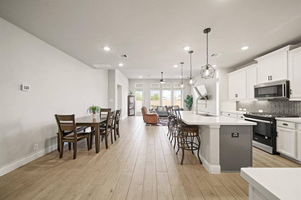 This photo showcases an open-concept kitchen and dining area with modern finishes. The kitchen features white cabinetry, a large island with seating, and pendant lighting. The dining area is spacious with ample natural light, leading to a cozy living space.