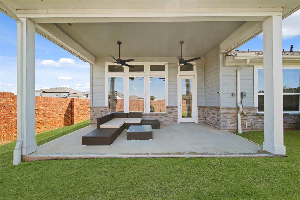 Spacious covered patio with modern outdoor seating, ceiling fans, and a brick wall for privacy—perfect for relaxation and entertaining.