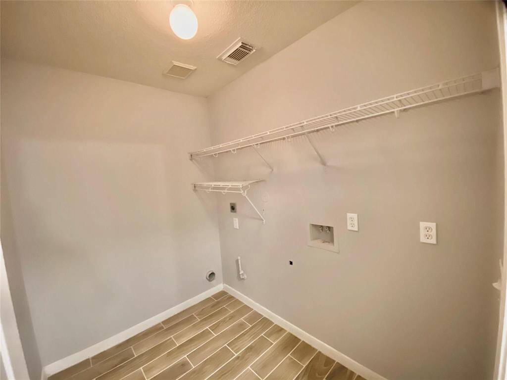 The laundry room with tiled flooring, neutral walls, and overhead wire shelving. It includes connections for a washer and dryer, with ceiling lighting.