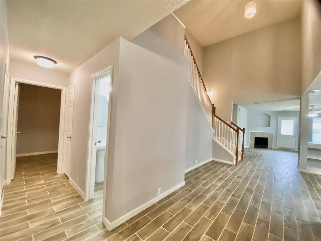 Bright and spacious home interior featuring a high ceiling, wood-look tile flooring, and a welcoming staircase. The open layout leads to a cozy living area with a fireplace, perfect for family gatherings.