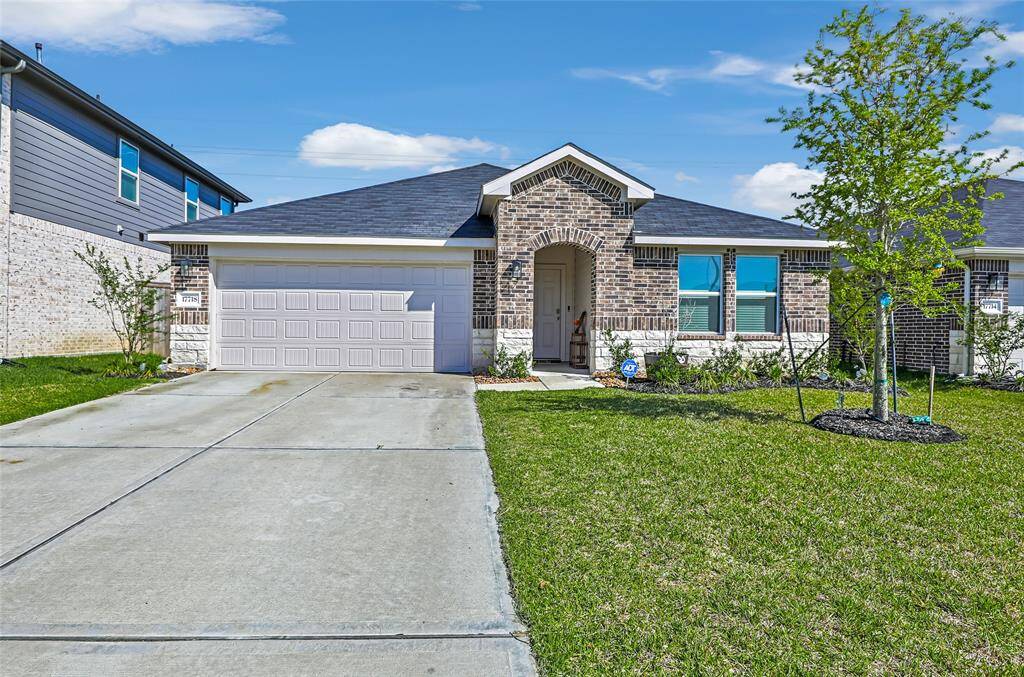 This is a modern, single-story brick home with a two-car garage. It features a well-maintained front yard with a few young trees and shrubs. The house has a welcoming entrance with an arched doorway and multiple windows, allowing natural light inside.