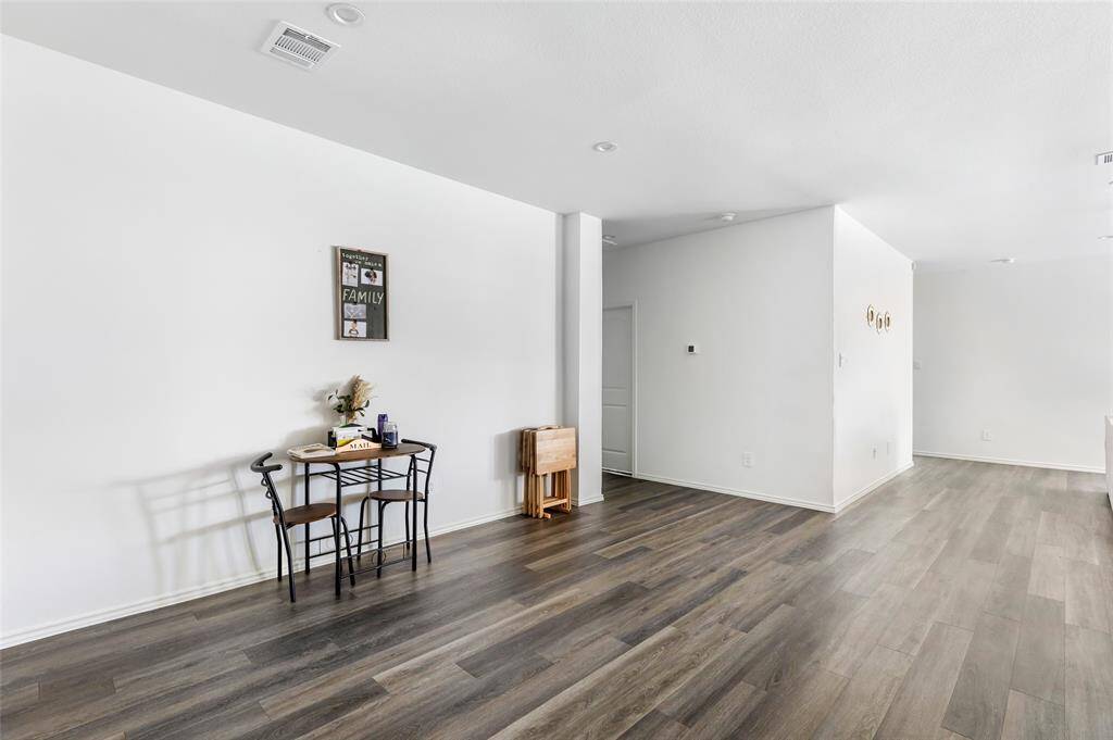 Spacious, open-concept living area with sleek wood flooring and bright white walls. The space includes a cozy dining nook with a small table and chairs, creating a welcoming atmosphere.