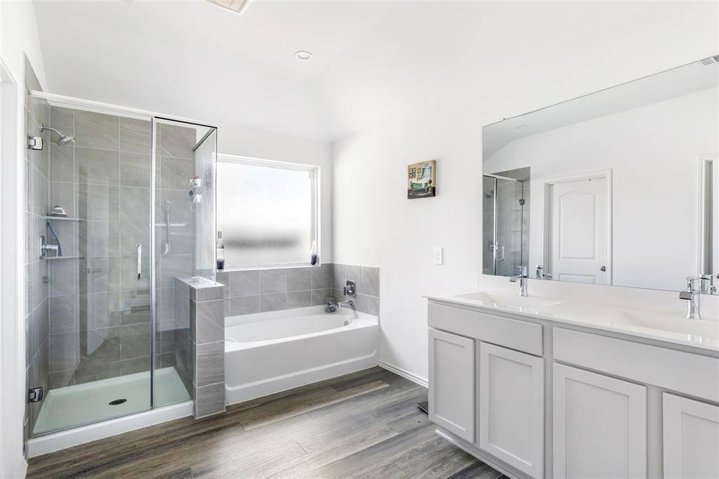 This bathroom features a modern design with a glass-enclosed shower, a separate bathtub, dual sinks with a large mirror, and sleek flooring, creating a bright and spacious atmosphere.