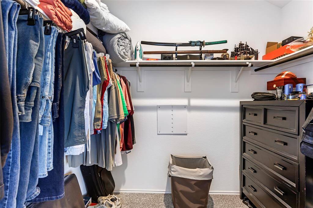 This is a spacious walk-in closet with hanging space for clothes, a shelf for storage, and a chest of drawers. The neutral carpet and walls create a clean, organized feel.