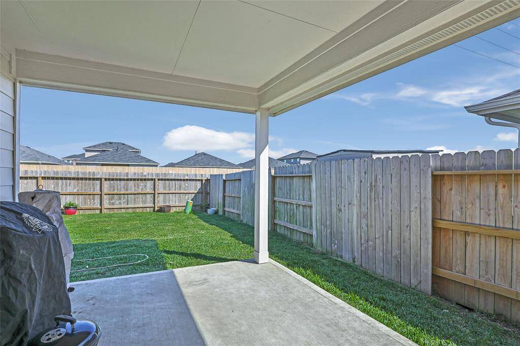 This photo shows a cozy backyard with a covered patio, perfect for outdoor relaxation. The space features a grassy lawn and a wooden fence for privacy, ideal for small gatherings or gardening.