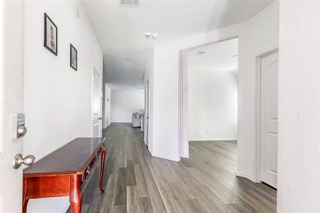This photo showcases a bright hallway with modern flooring, white walls, and recessed lighting. It features a wooden console table and leads into an open living area, creating a welcoming and spacious entrance.