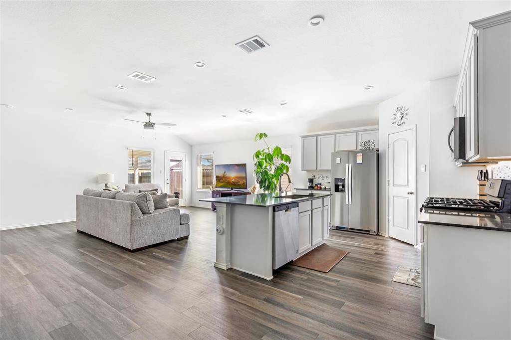 This open-concept living area features a modern kitchen with stainless steel appliances, an island with seating, and sleek cabinetry. The space flows into a cozy living room with ample natural light, complemented by light wood flooring and neutral decor.