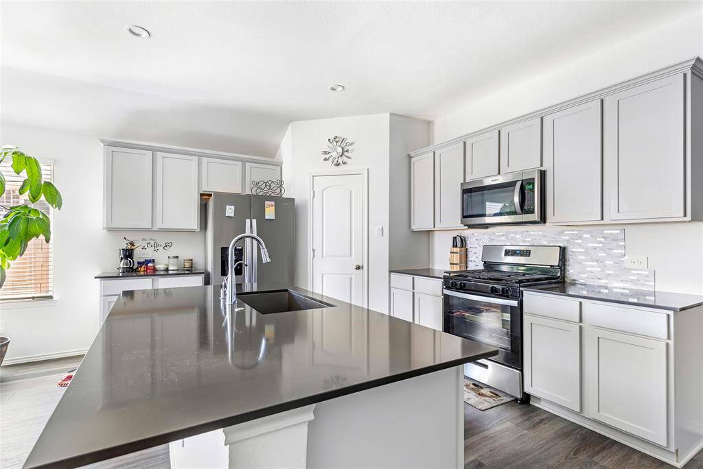Modern kitchen with sleek gray cabinets, stainless steel appliances, and a stylish island with a sink. Bright and airy with natural light from a nearby window.
