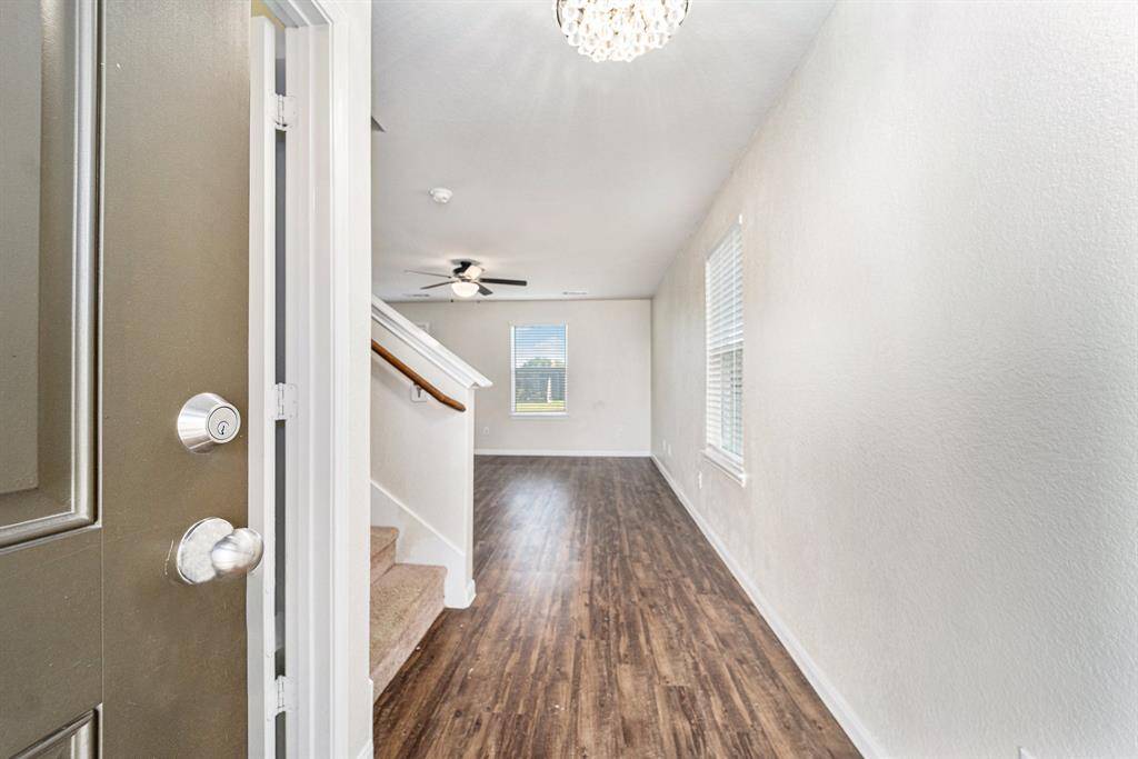 Welcome to a bright and inviting entryway featuring wood-look vinyl plank flooring, neutral walls, and a ceiling fan. The space is enhanced by natural light from the large windows. A carpeted staircase leads to the upper level.