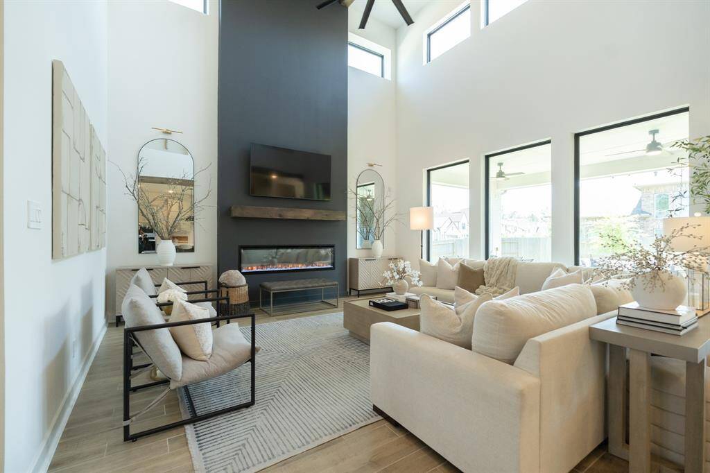 This spacious, modern living room is filled with natural light, thanks to soaring ceilings and expansive windows that invite the outdoors in. Designer Detail - custom painted windows and fireplace facade; wood beam-style mantle. Note - select furnishings may be available for purchase