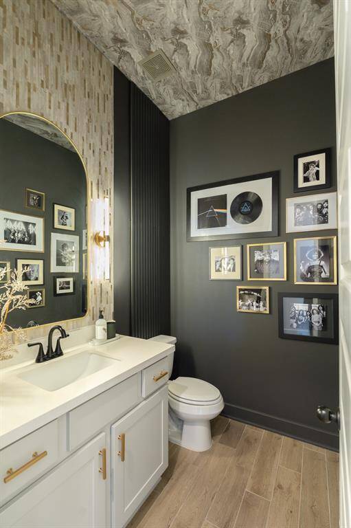 The Designer's vision is on full display in this GORGEOUS power bath! From the  vertical band of beige and gold mosaic tile that introduces a refined, textural element to the powder room, beautifully contrasting with the dark gray walls, to the wallpaper adorning the ceiling, adding depth and visual interest to the space.