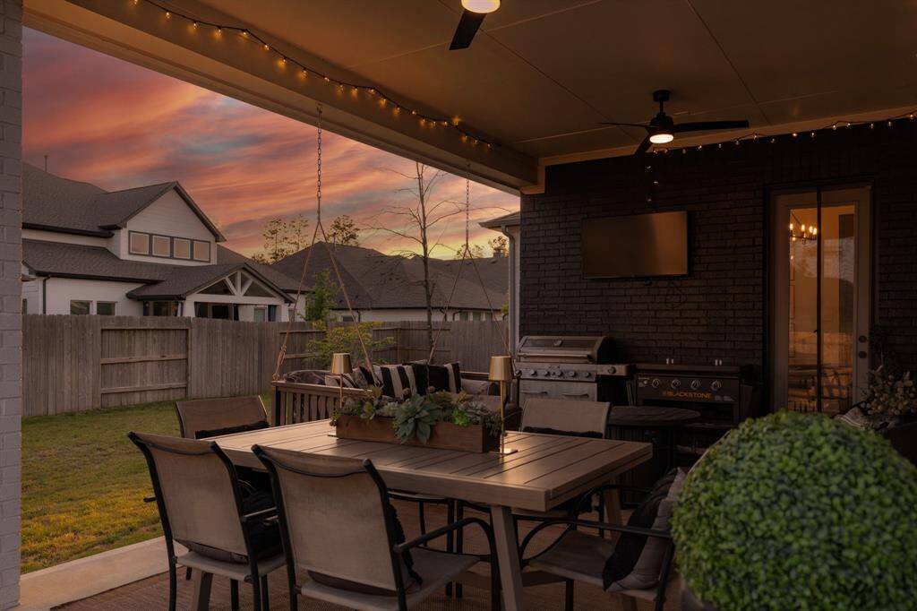 A spacious covered patio with ceiling fans and a stylish feature wall offers the ideal space for outdoor living and entertaining. Designer detail - custom paint accent wall. The dark brick wall adds a touch of sophistication, creating a rich, inviting atmosphere in the space. Note the flexible screen door - perfect for a breezy day!