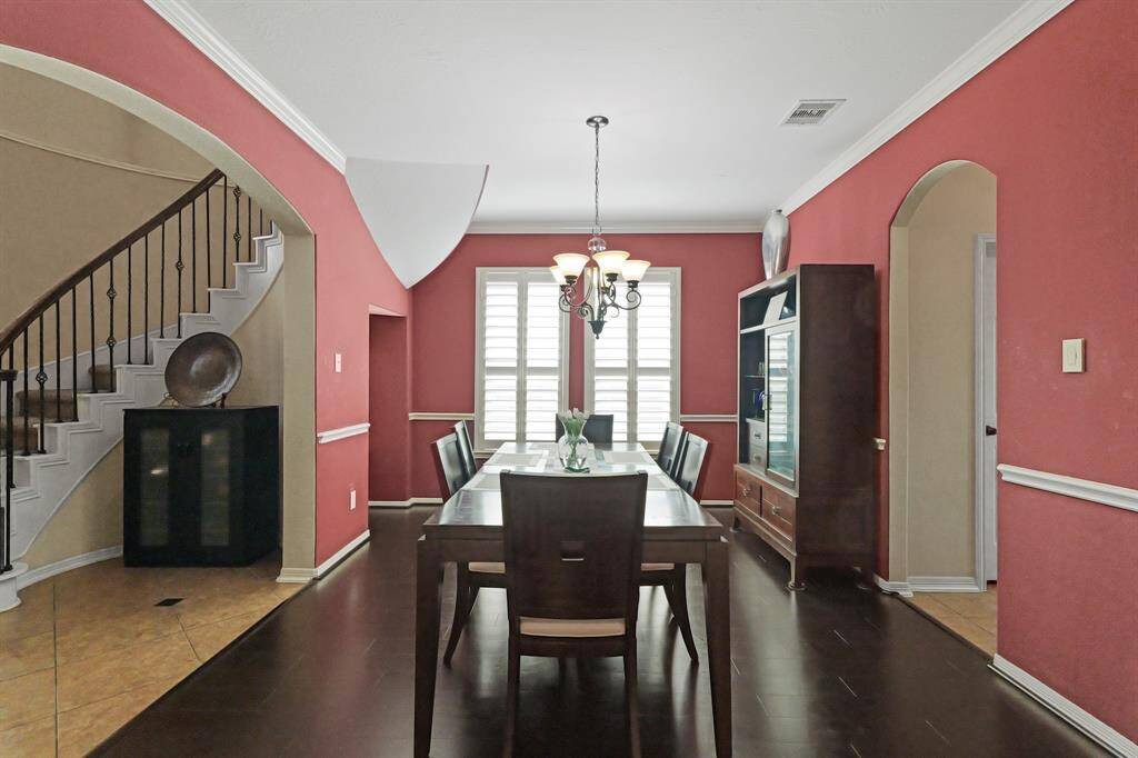 Spacious dining room with pendant lighting, crown molding details, windows with shutters, and tile floors.