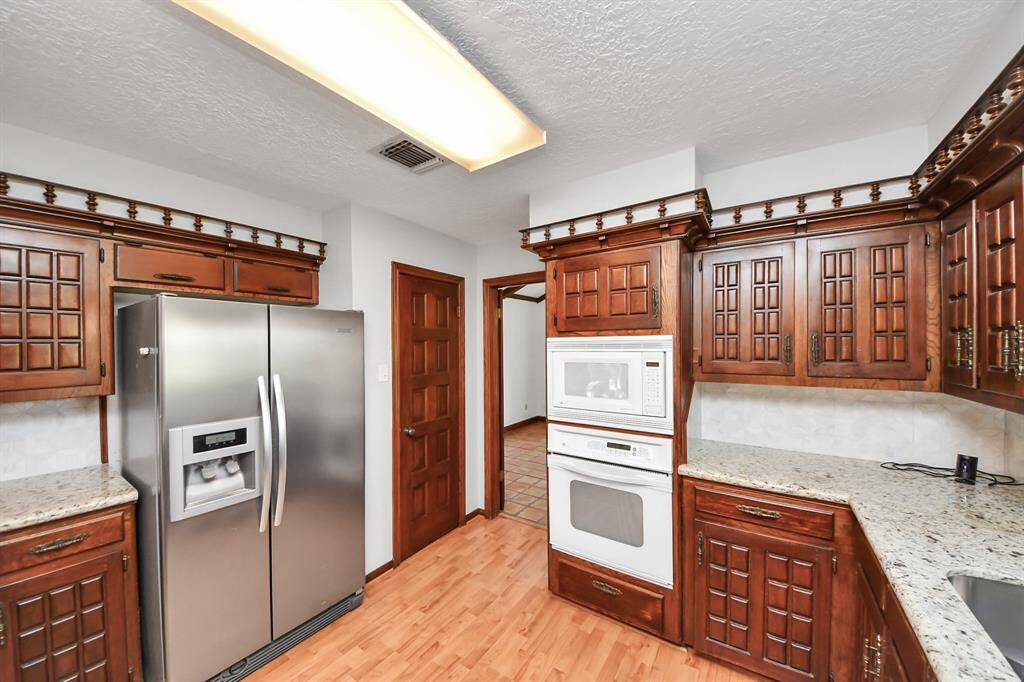 This functional kitchen features solid wood cabinets, granite countertops, a classic tile backsplash, and durable wood laminate flooring—combining style and practicality.