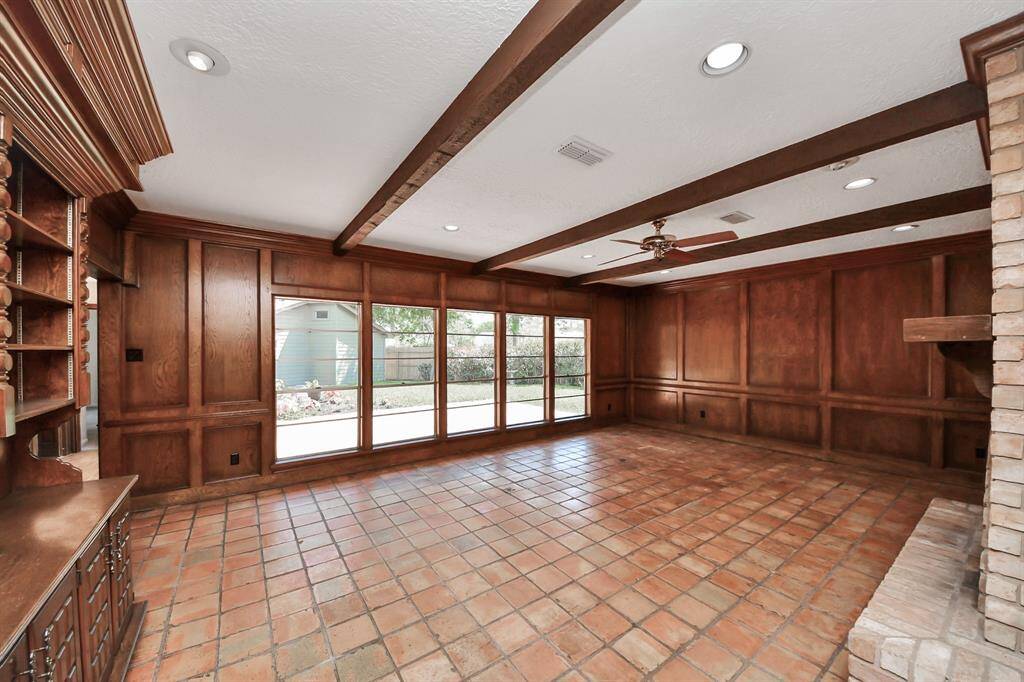 Saltillo tile extends into the den, where exposed beams add warmth and character, while a wall of windows offers stunning views of the beautiful, sizable backyard.