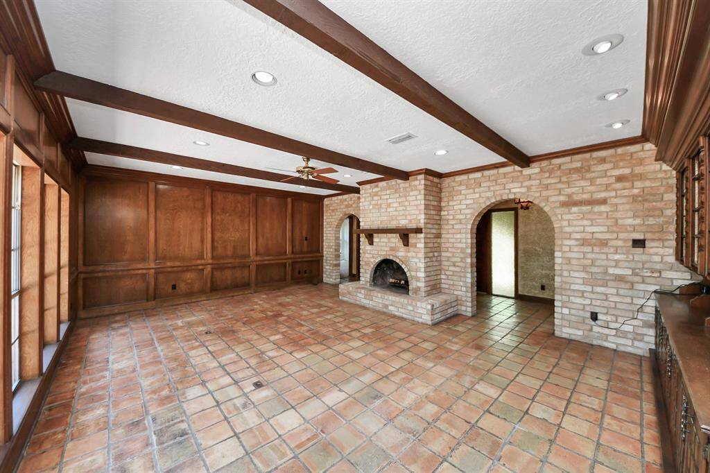 The rich, solid wood-paneled walls and brick hearth fireplace with wood mantle enhance the cozy yet spacious feel of this room, creating a warm and inviting atmosphere.
