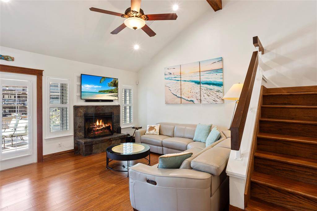 The living area boasts vaulted ceilings, wood beams, recessed lighting, and a cozy fireplace—perfect for relaxing evenings. French doors with wood-cased trim open to a lovely outdoor space, while plantation shutters add a classic touch.