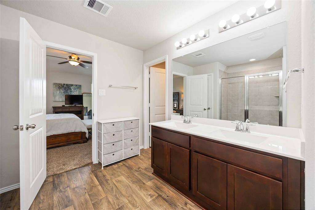 The primary bathroom features elegant double sinks, rich wood cabinetry, and stylish wood-look flooring.