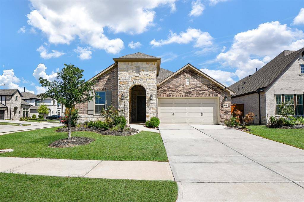This is a charming single-story home with a brick and stone exterior. It features a two-car garage, a well-maintained front yard, and a welcoming entrance. The neighborhood appears to be quiet and residential.