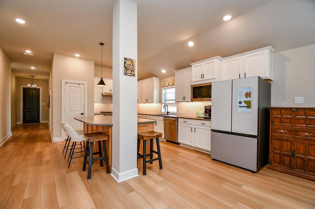 This modern kitchen features sleek white cabinetry, stainless steel appliances, and a stylish breakfast bar with seating. The open layout and wood flooring create a warm, inviting space perfect for cooking and entertaining.