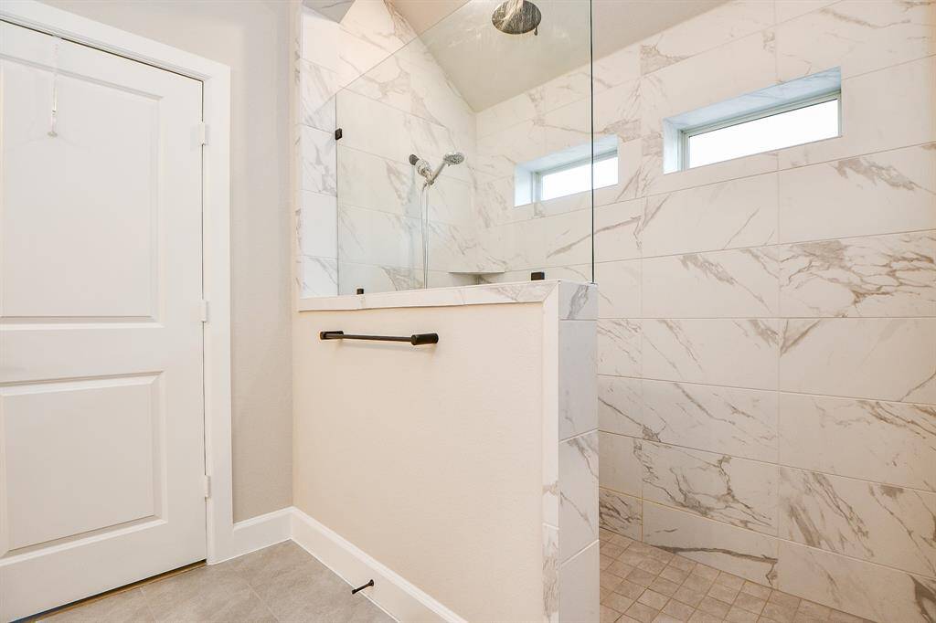 This photo shows a modern bathroom with a spacious walk-in shower featuring elegant marble tiles and dual windows for natural light.
