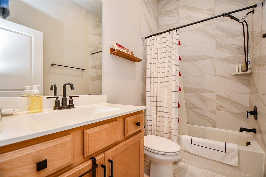 This bathroom features a modern design with a sleek vanity, black fixtures, and a large mirror. The shower area has elegant tile work and a stylish curtain, creating a fresh and inviting space.