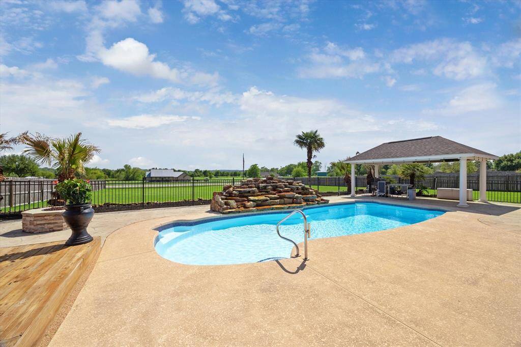 A view of the beautiful pool complete with a large, tranquil waterfall, a corner of the deck, the firepit, and massive fenced-in back yard. And the covered area is ready for that brand new outdoor kitchen that is ready to be included with the sale of the house and to be installed by the buyer.