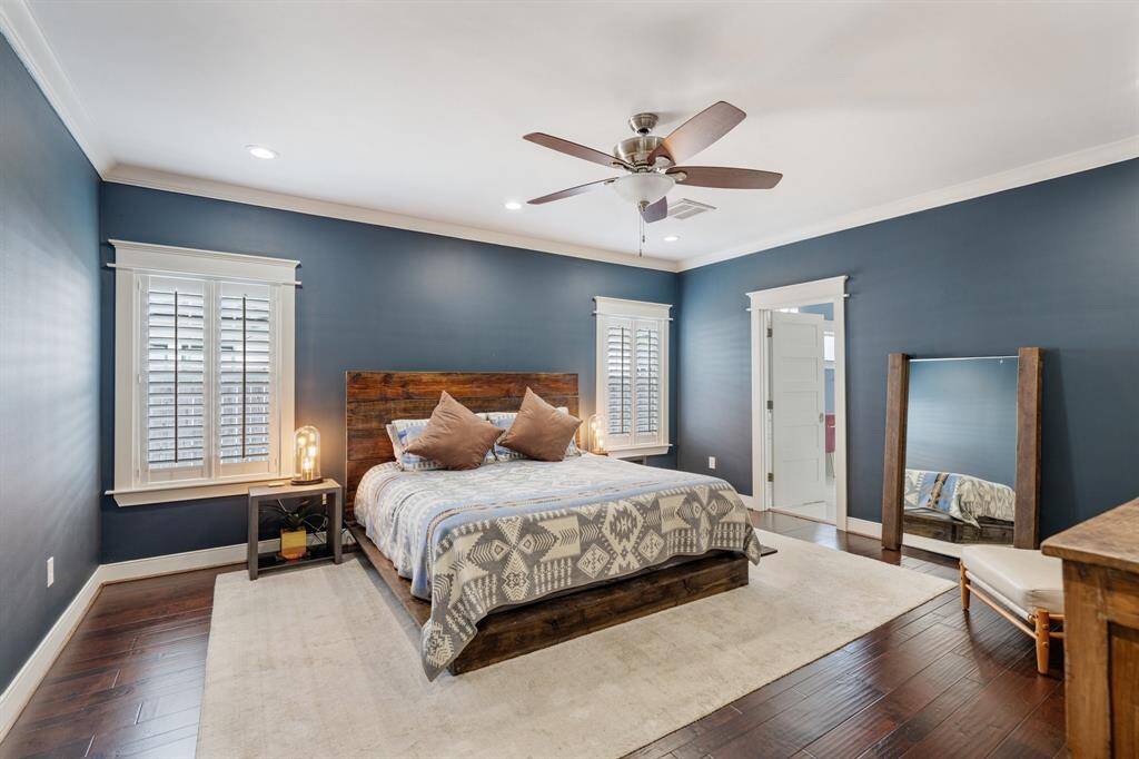 The primary suite, conveniently located on the first floor, features a spacious bedroom with plantation shutters and rich hardwood floors. Its elegant crown molding and thoughtful layout make it an inviting sanctuary.