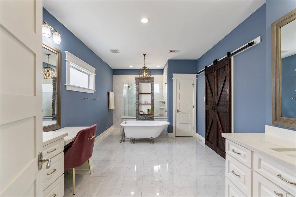 This spa-like primary bathroom offers a clawfoot soaking tub, a spacious walk-in shower, and elegant marble flooring. A stunning blend of rustic and modern elements, including a sliding barn door and stone accents, creates a refined retreat.