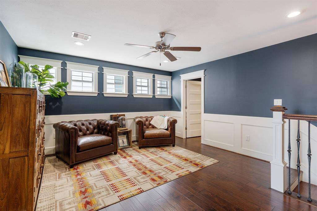 This inviting second-floor landing serves as a versatile space, featuring elegant wainscoting, rich hardwood floors, and ample natural light from a row of windows. Its open design makes it perfect for a reading nook, workspace, or additional lounge area.