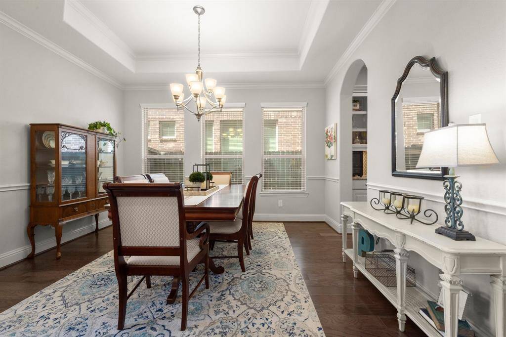 The formal dining room features three large windows that allow natural light to pour in, enhanced by elegant blinds. A tiered ceiling with crown molding and a beautiful chandelier creates a sophisticated space for entertaining.