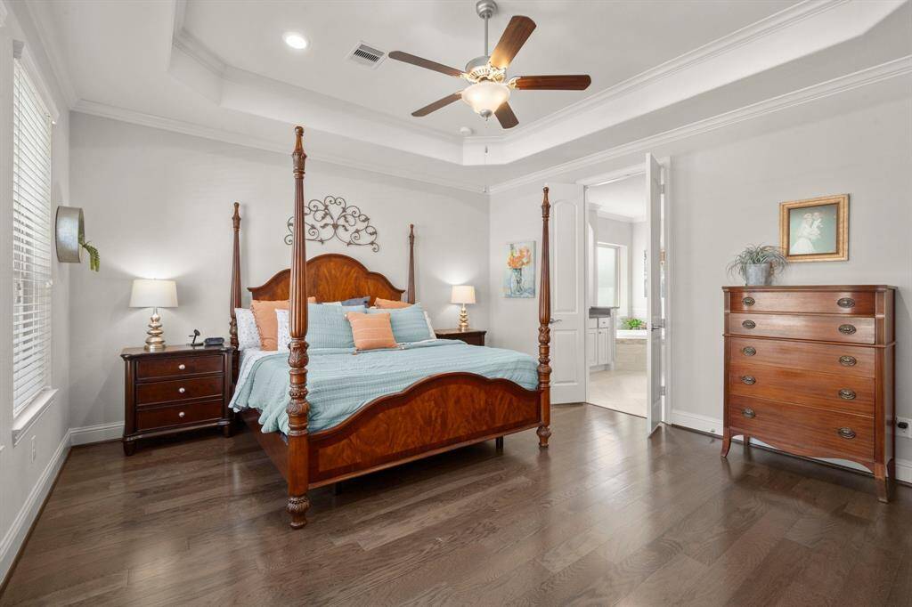 The primary suite is a true sanctuary with a tiered ceiling, ceiling fan, and rich hardwood floors throughout.