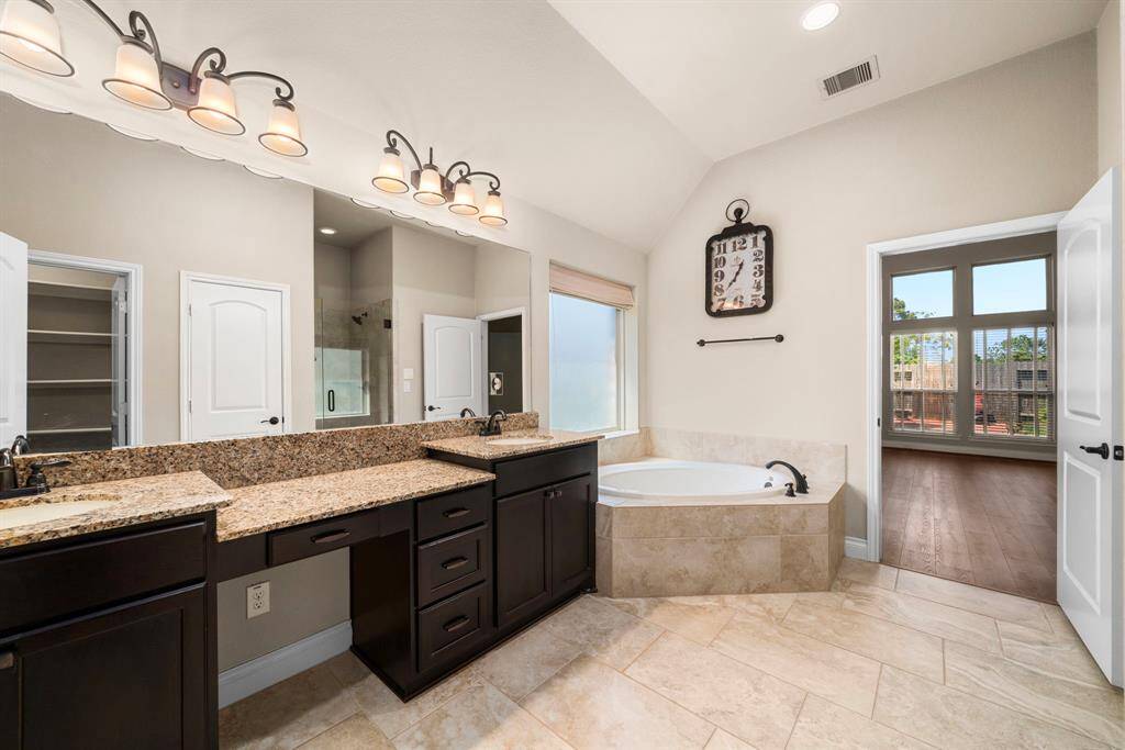 The spa-like primary bathroom features a large corner soaking tub and separate vanities with granite countertops. A makeup area, framed mirrors, and a walk-in shower round out the elegant design.