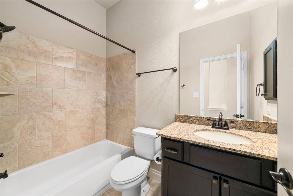 The guest bathroom offers a modern look with a granite vanity, undermount sink, and a tiled shower/tub combo. Thoughtfully designed with durability and style in mind.
