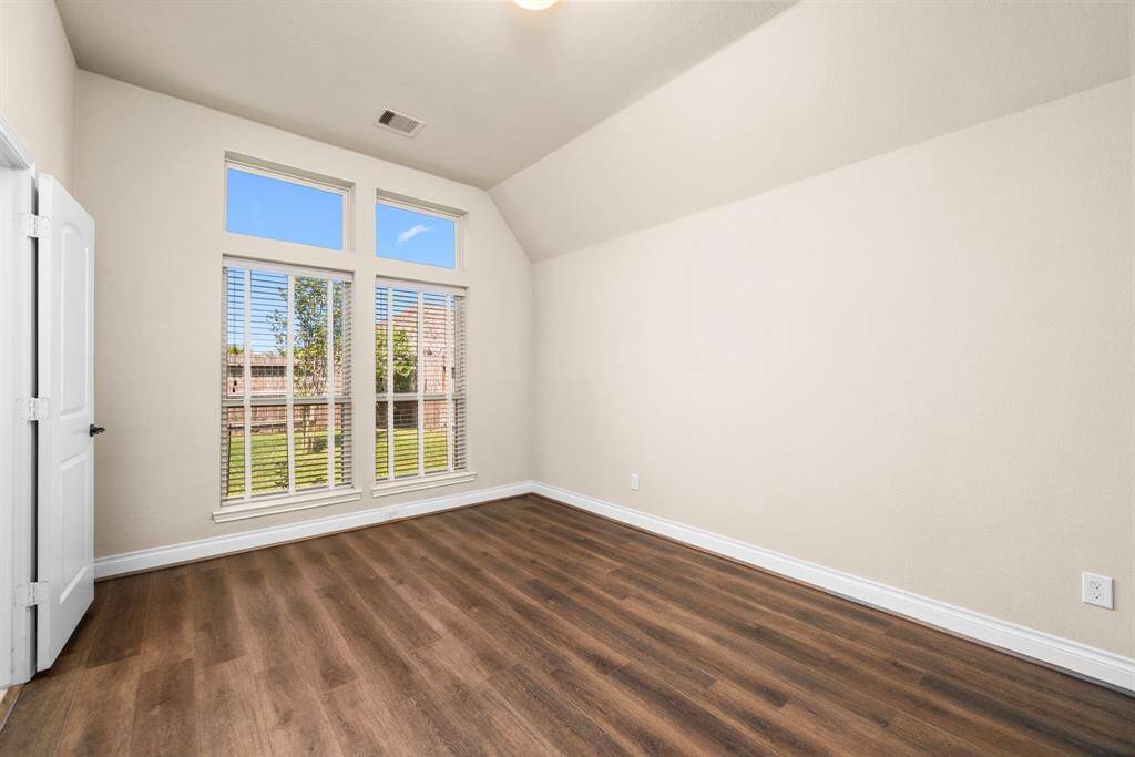 This secondary bedroom offers ample space and natural light with its large windows overlooking the backyard. Elevated ceilings and wood-look flooring provide a clean, modern backdrop for any décor style.