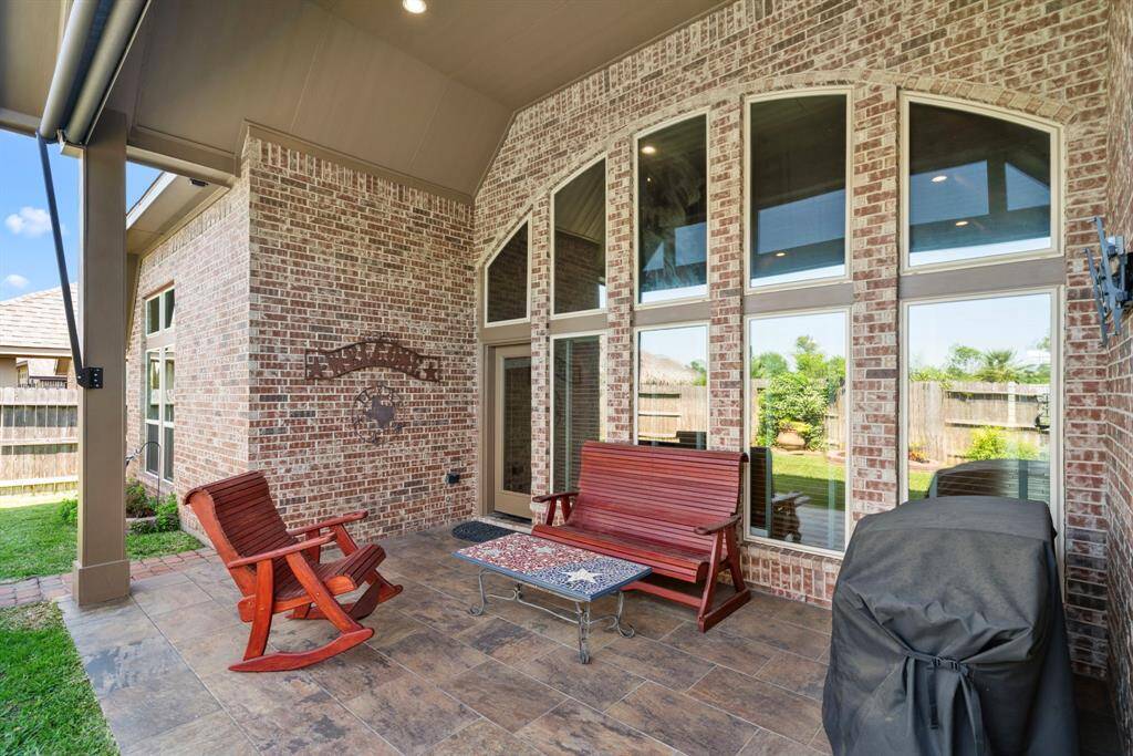 The extended covered patio is the perfect spot to unwind or entertain, featuring tile flooring and recessed lighting. A wall of brick and windows adds architectural charm and visual interest.
