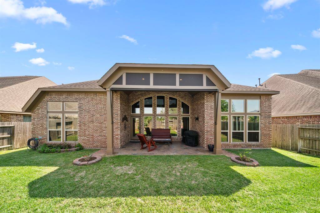 A full rear view of the home showcases the beautifully arched brickwork and towering windows. The covered patio and manicured lawn make this outdoor space a true extension of the home.