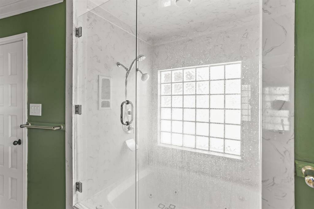 It highlights a beautiful glass enclosed shower/tub combo and a large window with privacy glass providing natural light.