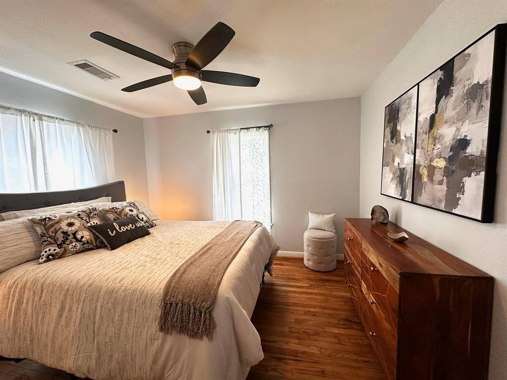 Primary bedroom features updated ceiling fan, a queen size bed, night tables and solid wood dresser.