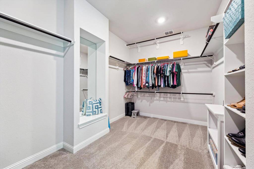 The primary closet is an incredible space featuring a  full length mirror, built in storage and expansive space for clothing.