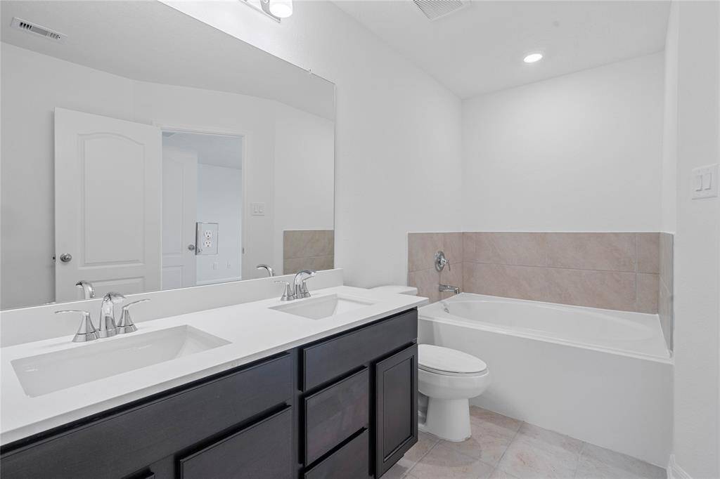 This primary bathroom is definitely move-in ready! Featuring an oversized tub with tile surround, stained cabinets with light countertops and dual vanities, mirror, high ceilings, custom paint, sleek and dark modern finishes.