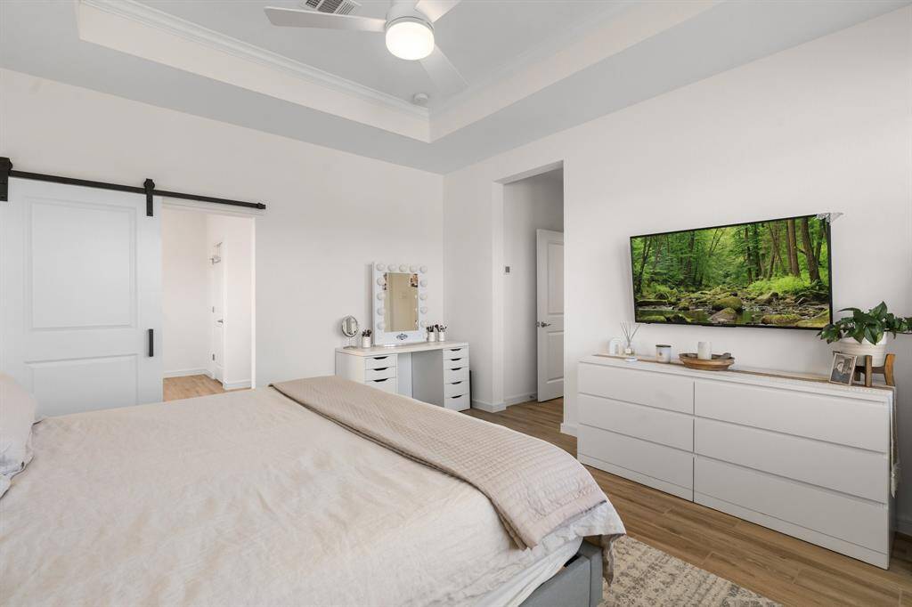 Bright and airy primary features a tray ceiling and a sliding barn door leading to an adjoining ensuite bath.
