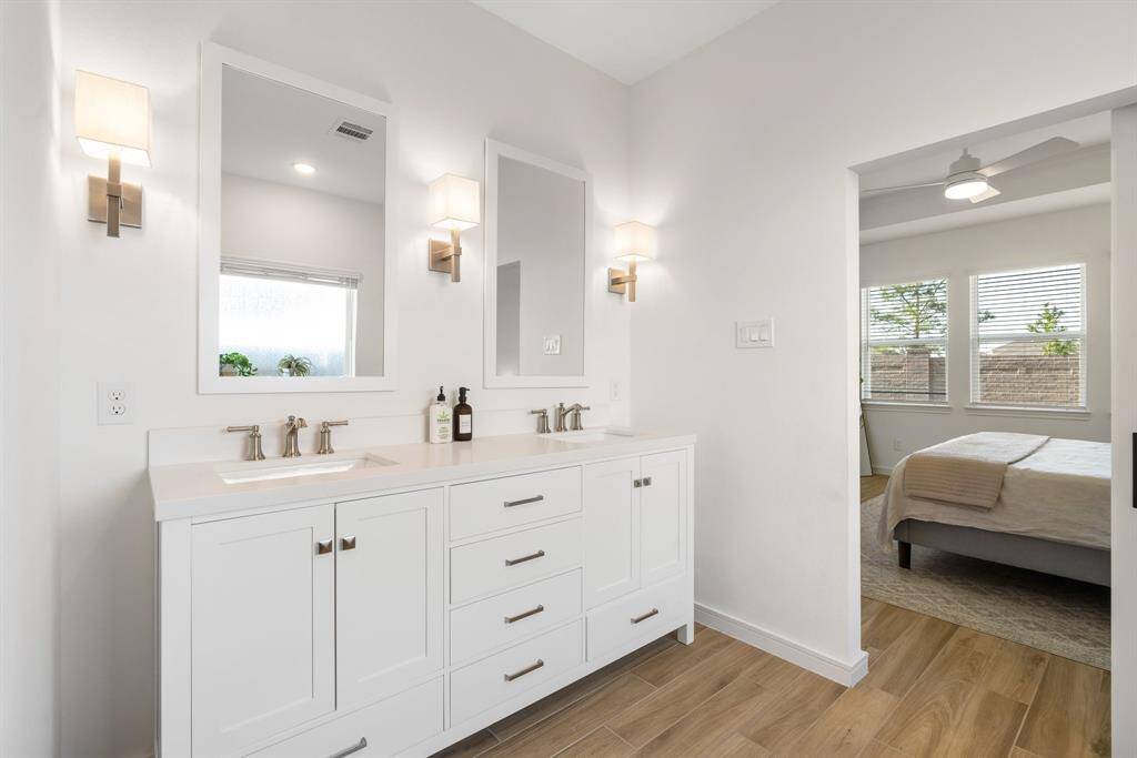 Modern bathroom with a dual-sink vanity, sleek fixtures, and ample storage. The space connects to a bright bedroom with large windows, offering natural light and a cozy atmosphere.