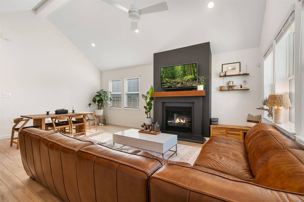 Bright, open living space with high ceilings and a cozy fireplace. Natural light fills the room through large windows, creating a warm and inviting atmosphere.