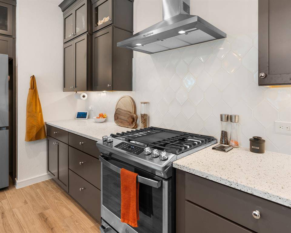 Modern kitchen with sleek dark cabinets and light countertops. Features include a stainless steel gas stove with griddle and a stylish hood and a white tile backsplash for a clean, contemporary look.