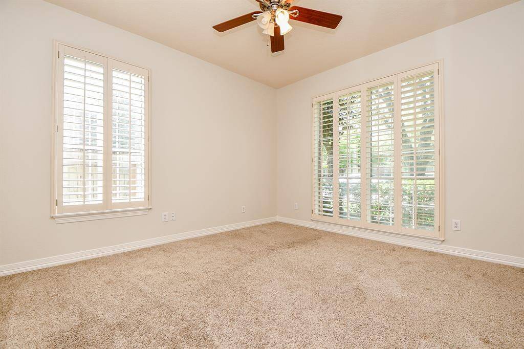Here's a bright and inviting study featuring elegant plantation shutters, plush carpeting, and a ceiling fan.