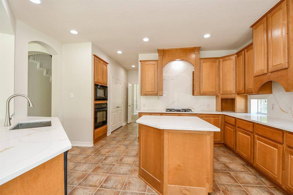 This kitchen features warm wood cabinetry, quartz countertops, central island, built-in oven and microwave, and modern lighting, offering a spacious and functional cooking area.